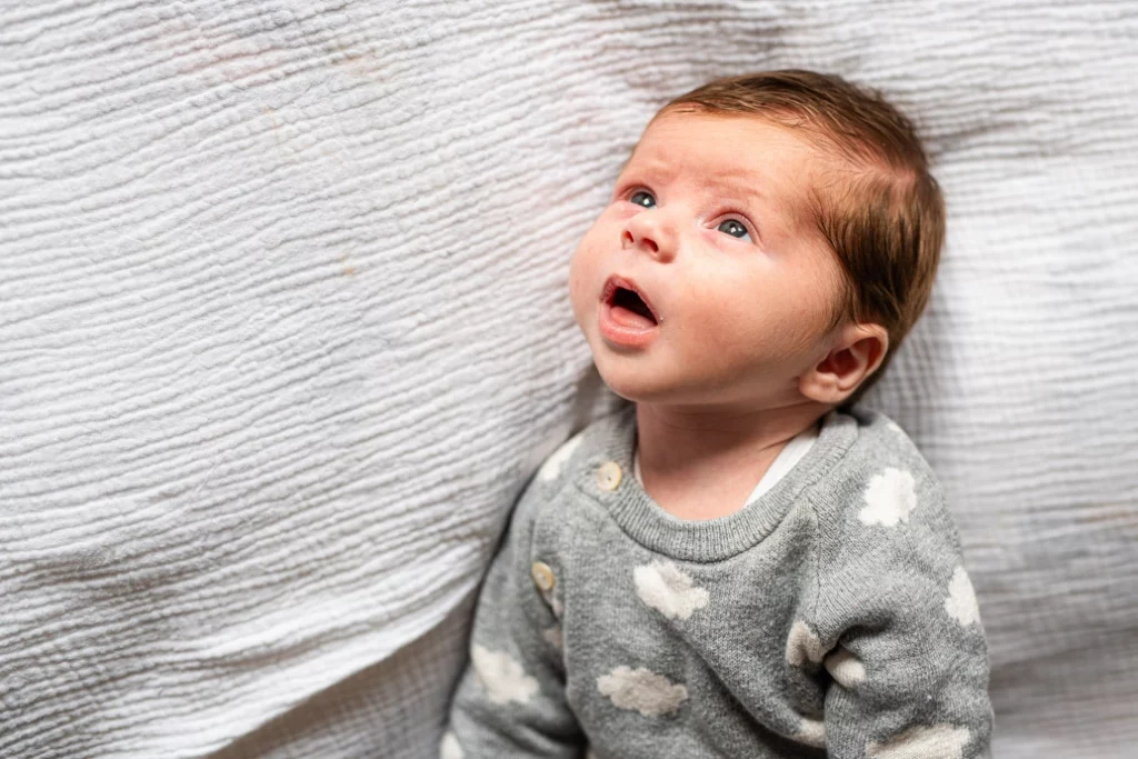 Séance photo bébé Igny, Nouveau-né allongé sur un lit qui regarde attentivement le plafond