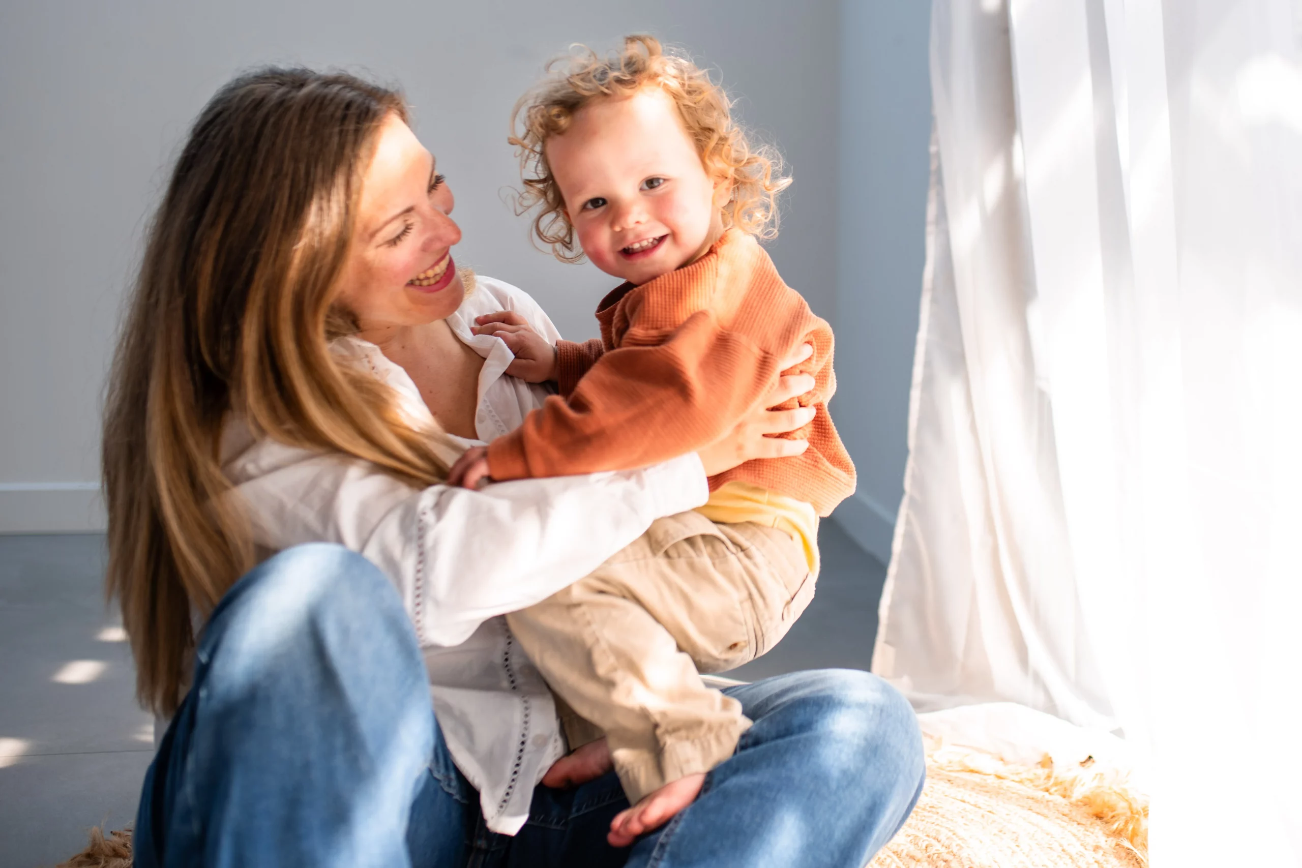 petit garçon souriant dans les bras de sa maman lors d'un shooting photo en studio
