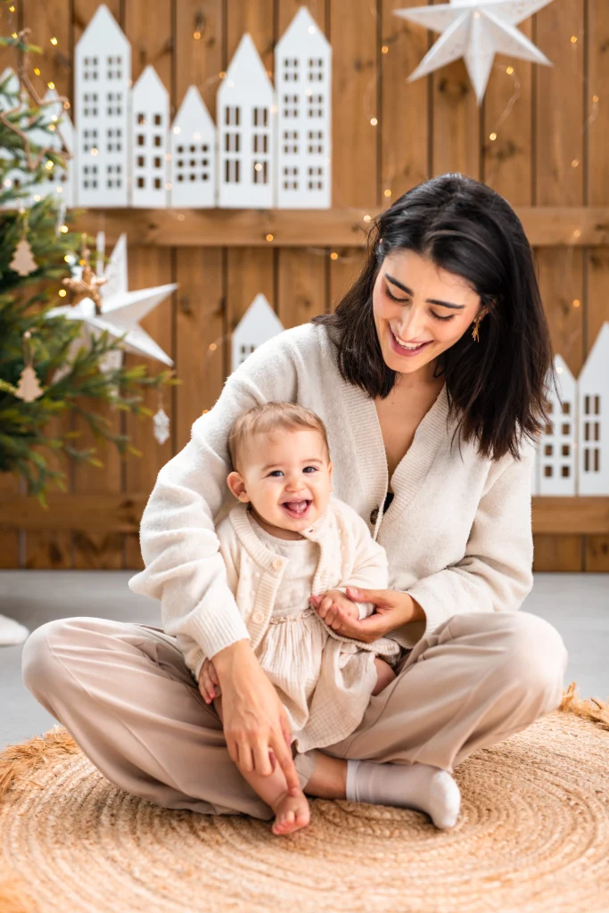portrait d'une maman avec son bébé souriant sur les genoux lors d'une mini séance photo de noël